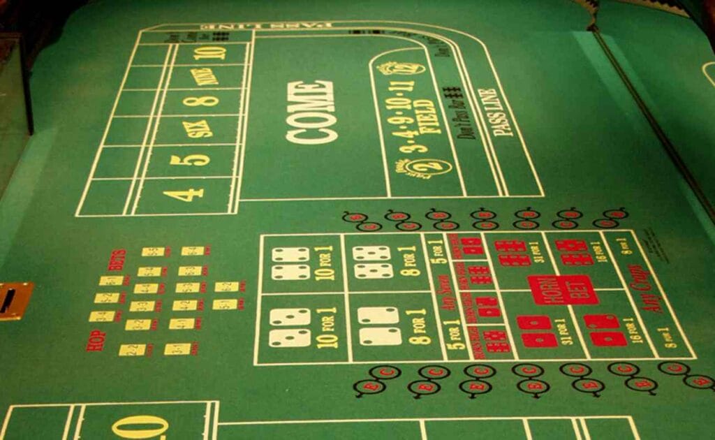 A close-up of a green felt craps table with the proposition bets in the foreground. The felt is covered with red and white words, as well as yellow numbers.