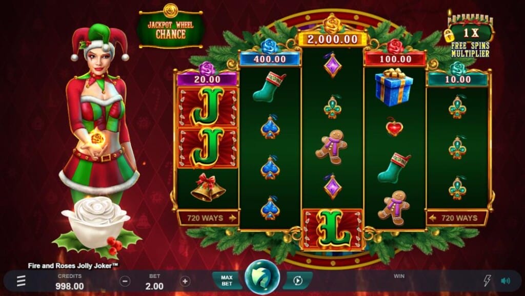 A screenshot of the slot reels in Fire and Roses Jolly Joker. The background is a red wall with various Christmas-themed symbols on it. In the foreground are the game reels in a 3-4-5-4-3 format. The reels are surrounded by evergreen leaves and feature a variety of slot symbols, including Christmas bells, stockings, gingerbread men, and presents, as well as playing card symbols in the style of jewelry. Above each reel are the various jackpot payouts. On the left is the game’s Joker mascot. She’s wearing a Christmas-themed outfit and has a ball of fire floating above her hand. Below her is a white rose with mistletoe. At the bottom of the screen is the game’s interface. 