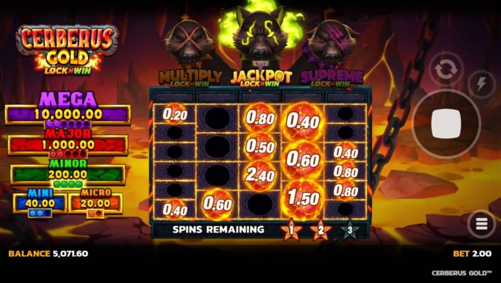 A screenshot of the Jackpot LockNWin feature in Cerberus Gold. The background is a rocky pit filled with orange lava and rocky outcroppings. In the foreground are the slot reels containing a mix of fireball symbols with cash payouts and empty reel positions. Above the reels are the three Cerberus heads with different colored markings. The jackpot LockNWin head with yellow markings and flames is highlighted. To the left of the reels are the five jackpots, and to the right of the reels, the game interface.