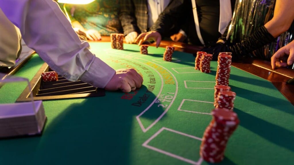 Dealer and players at a blackjack table with tall stacks of red casino chips in front of each betting spot.