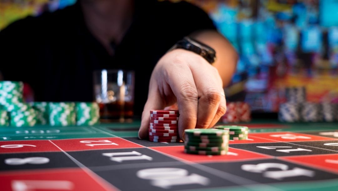 A close-up of a hand placing poker chips on a roulette table.