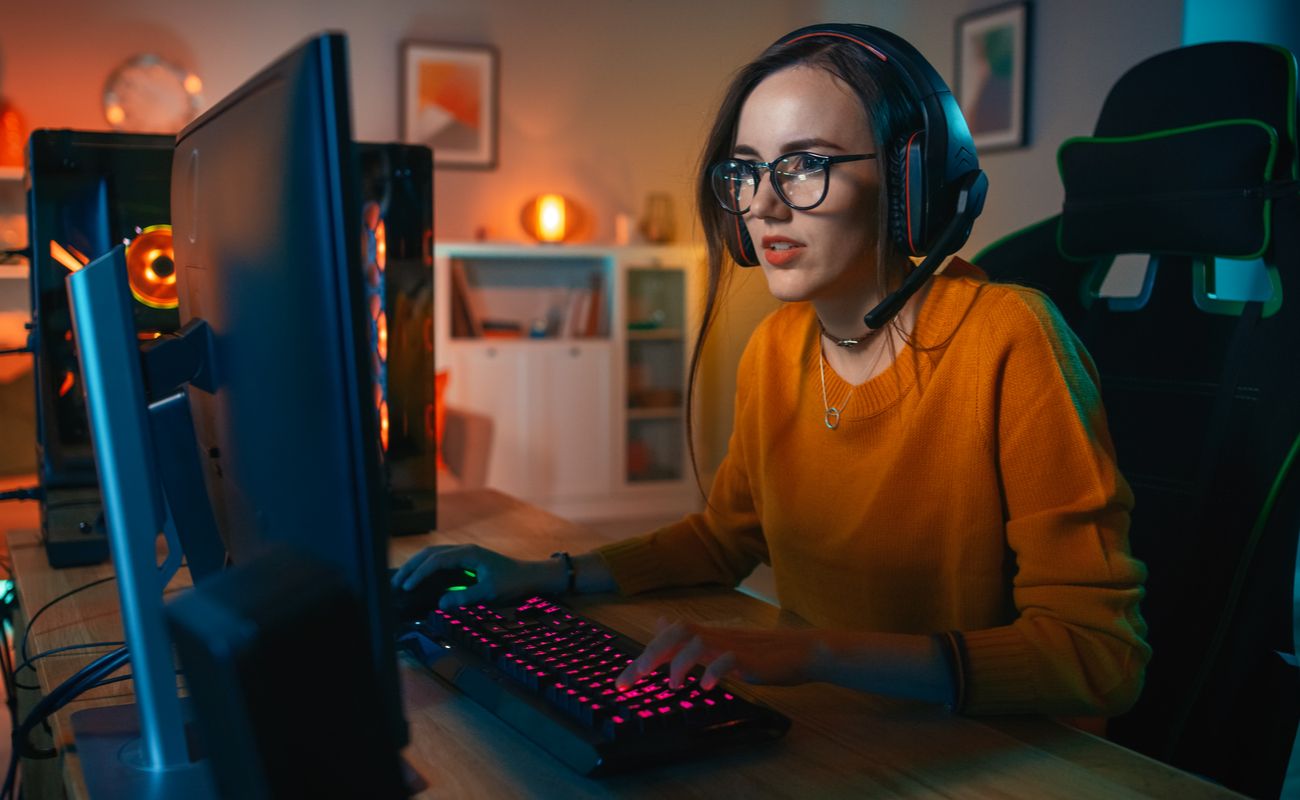 A girl staring at her monitor playing an online game on her desktop PC using a lit up mouse and keyboard.