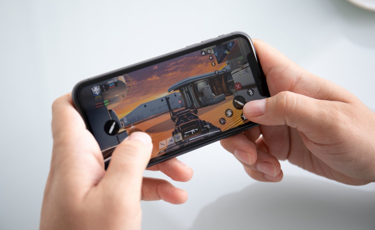 Pair of hands holding an iPhone in portrait mode playing Call of Duty with a white background.