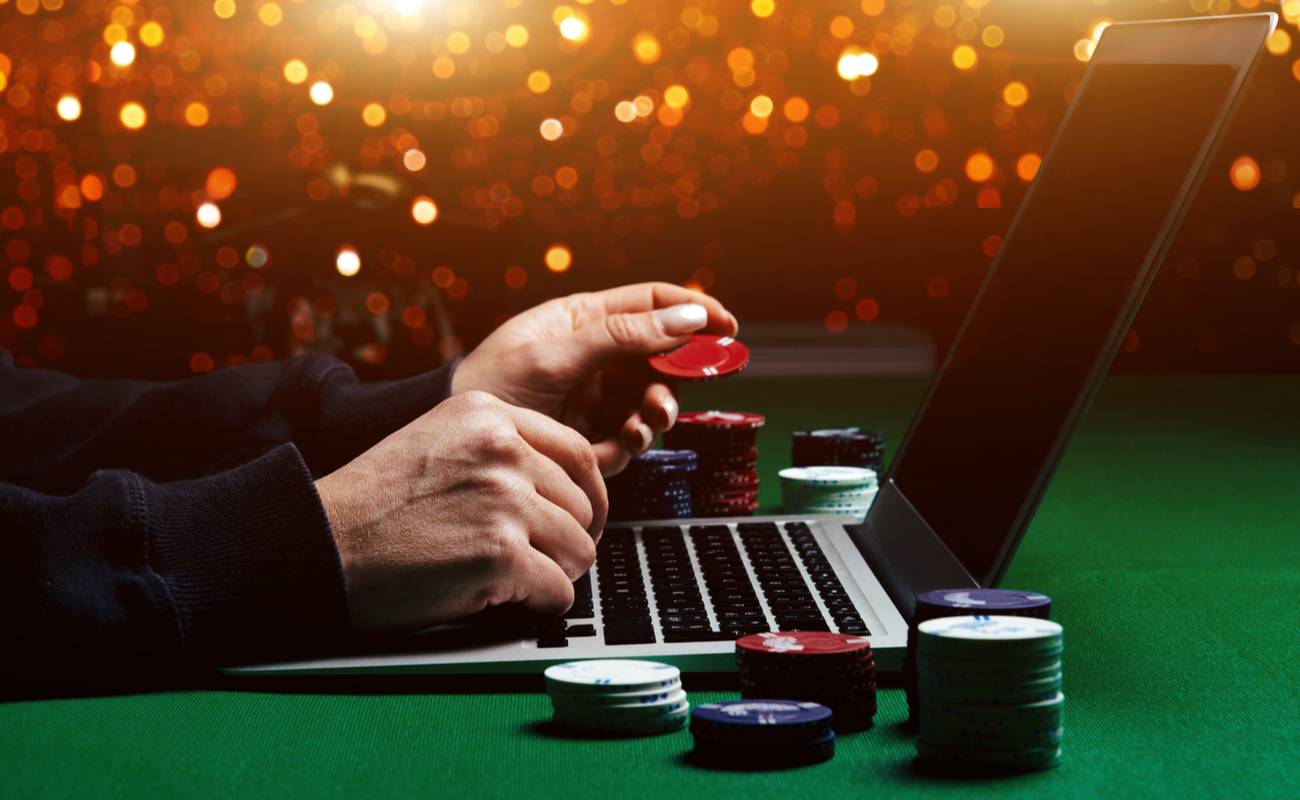 man holding casino chips in front of laptop for online poker