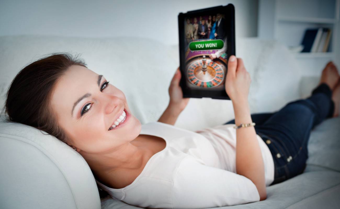 smiling woman lying on couch with tablet showing successful online gambling