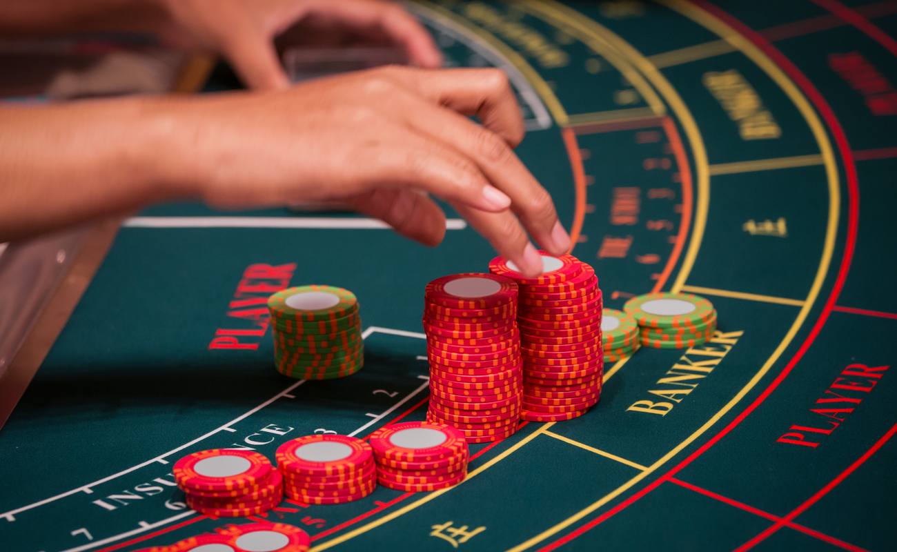 Someone playing baccarat on a green table with red and green poker chip stacks.