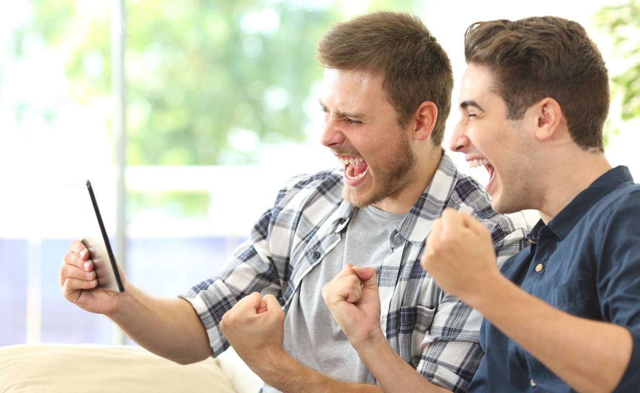 two men celebrating with their fists up whilst looking at a tablet