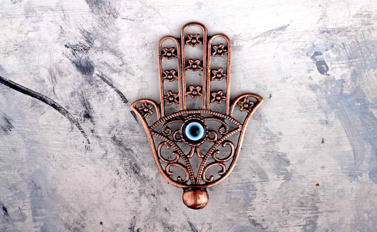 Golden Turkish Hamsa Hand Pendant with an evil eye bead in the center on concrete background