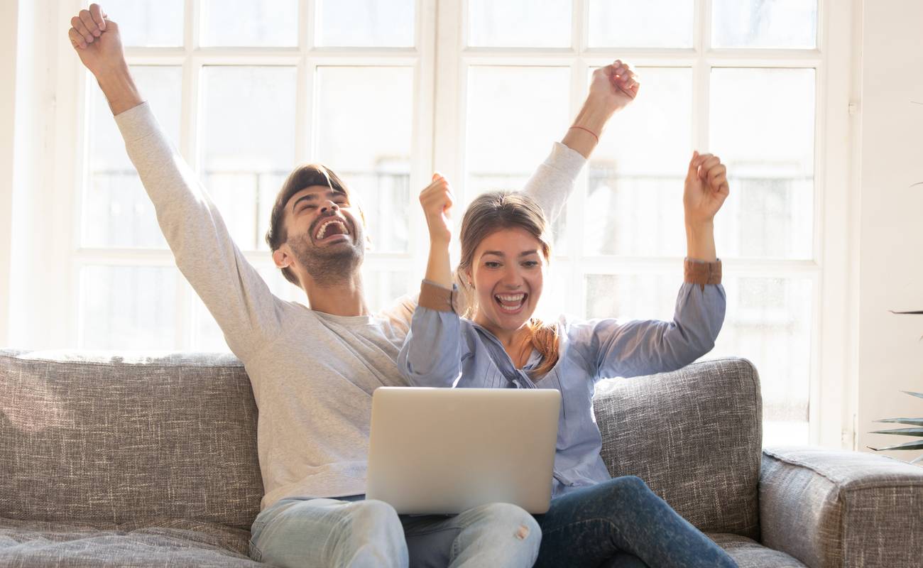 Happy young couple celebrate online victory, screaming with joy raising hands