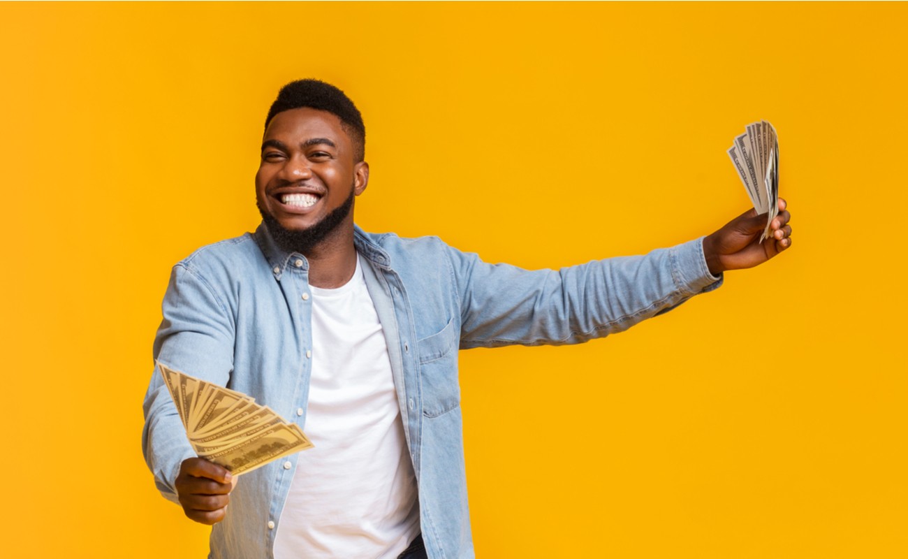 Overjoyed Man Holding Money In Both Hands On Yellow Background