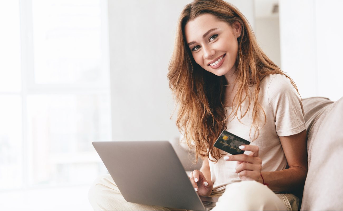 smiling woman showing credit card to the camera while on laptop