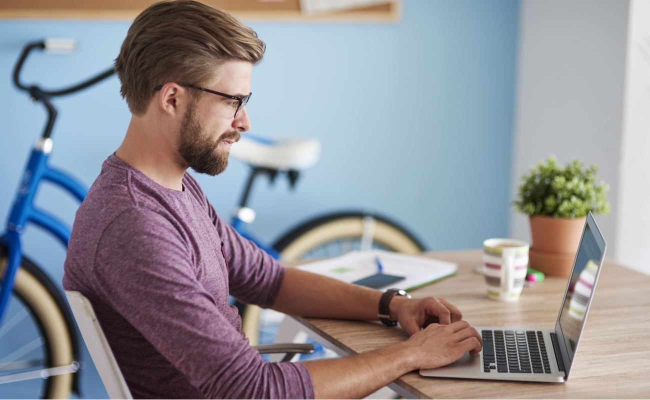Hipster man playing on laptop at home with bicycle in background