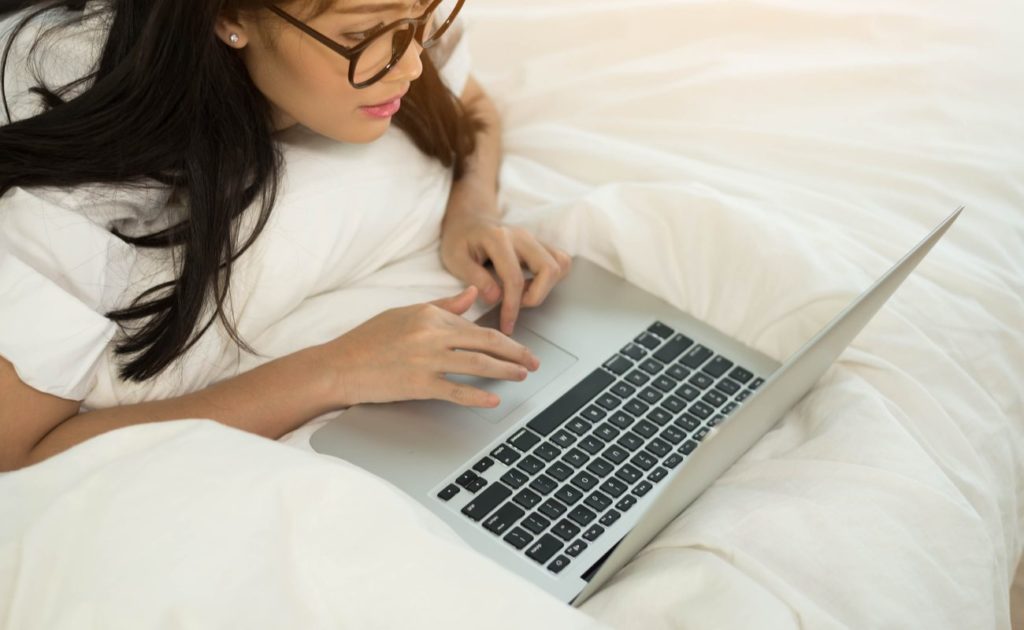 Woman scrolling on a laptop on a white bed