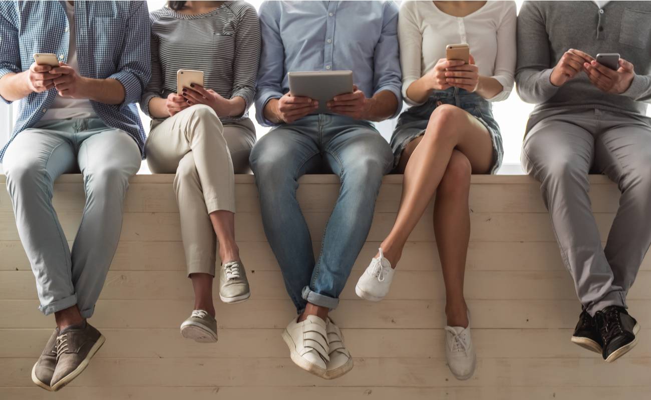 Row of people sitting on the wall with smartphones and tablets in their hands