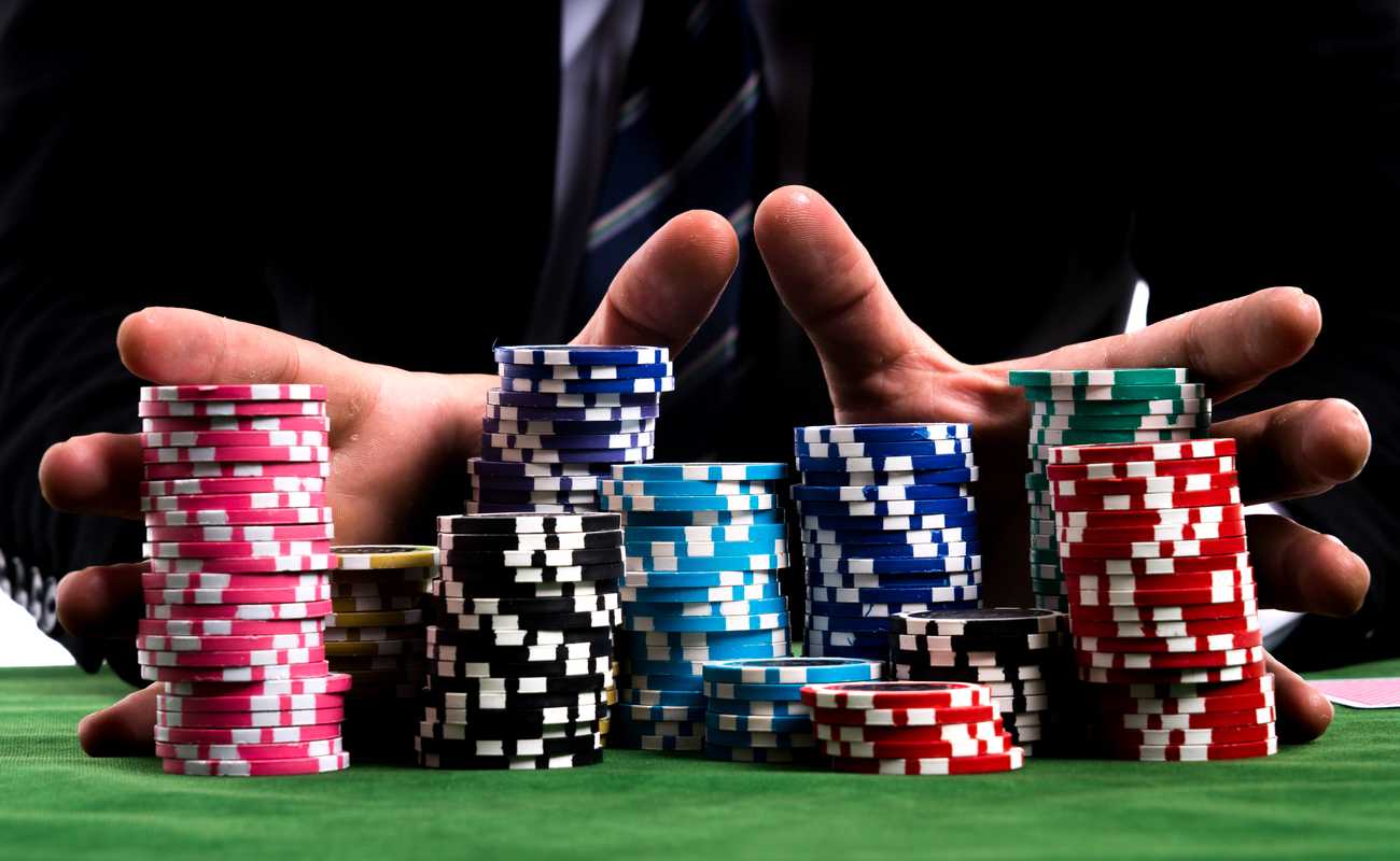 Close up of hands pushing large stack of colored poker chips across gaming table for betting