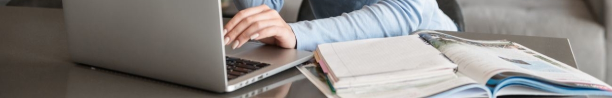 Close up of a woman working on a laptop with a book next to her