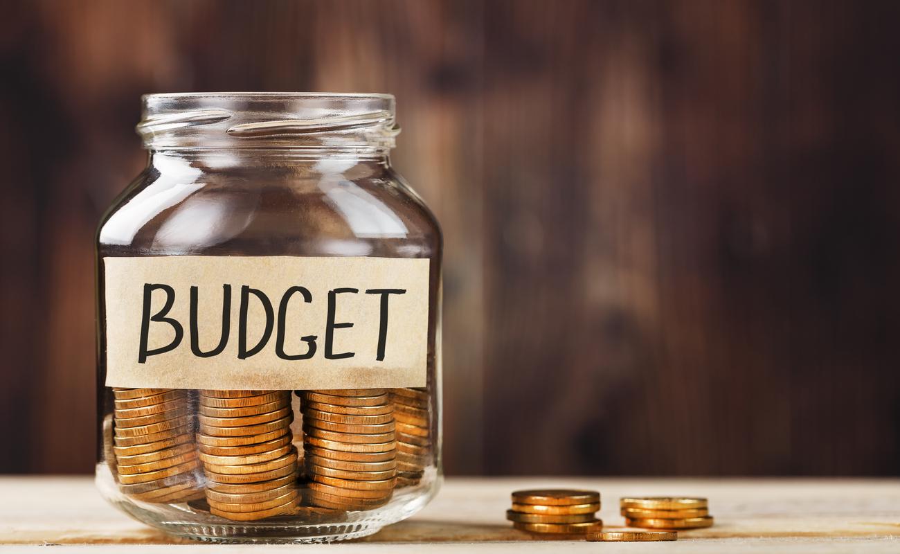 Glass jar with money and a sticker showing the words BUDGET, on a wooden table.