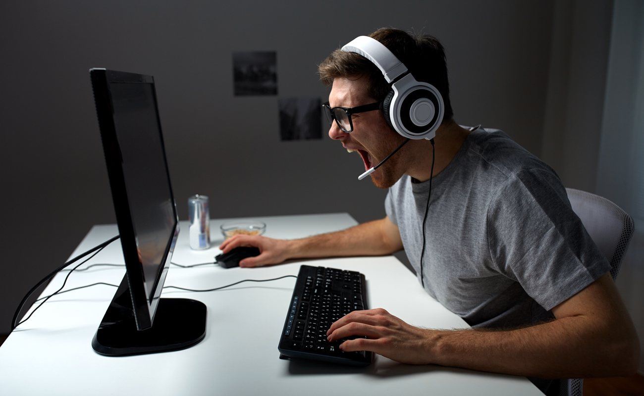 A PC gamer wearing a headset with a microphone shouts at the screen.