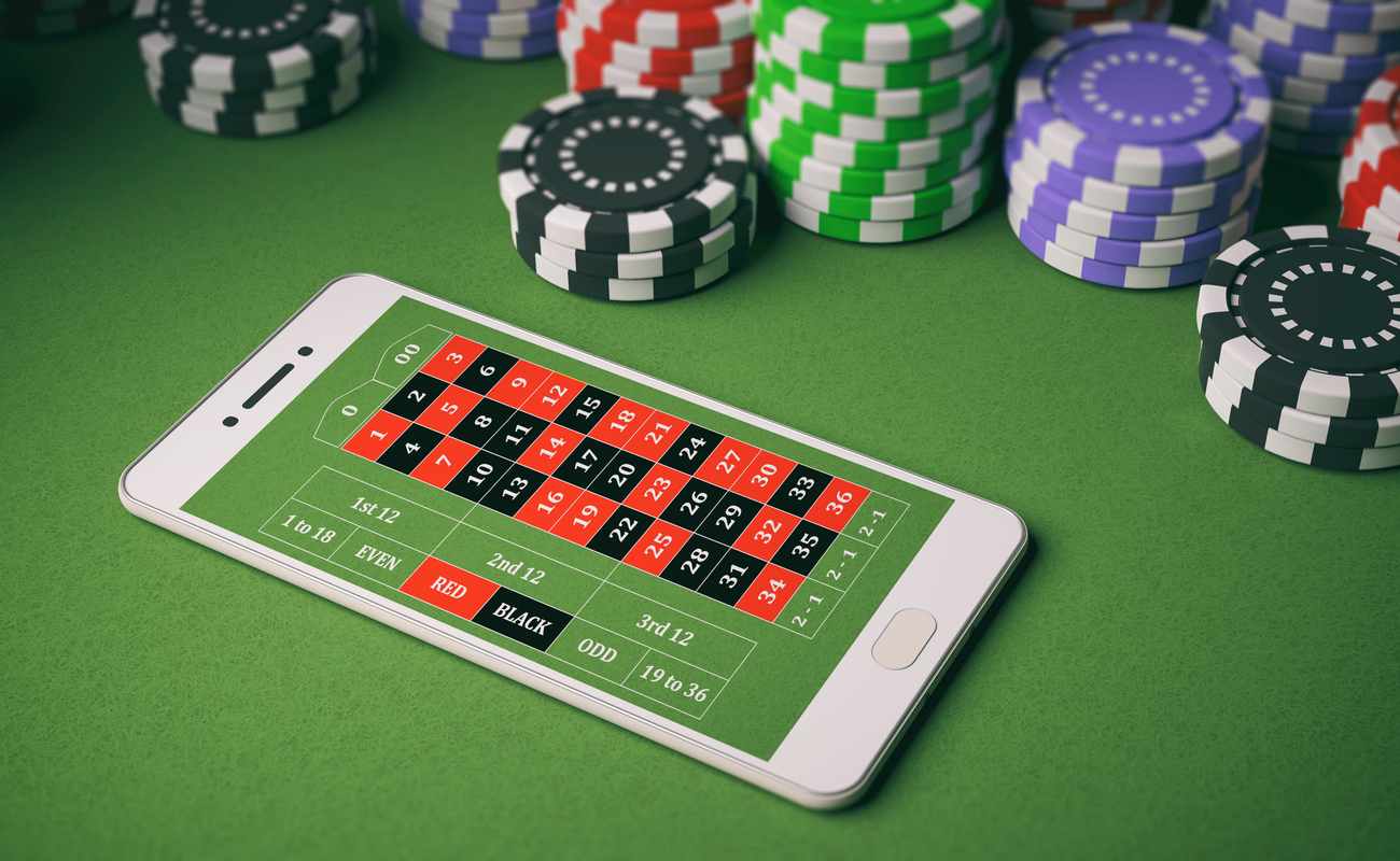 Casino table with poker chips and a white mobile phone displaying a roulette board.