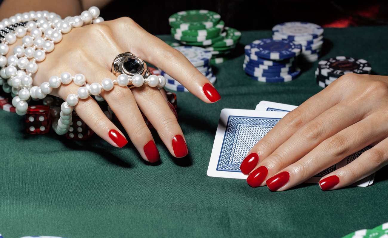 Woman's hands holding cards on a felt table, wearing a ring and pearl necklace bracelet.