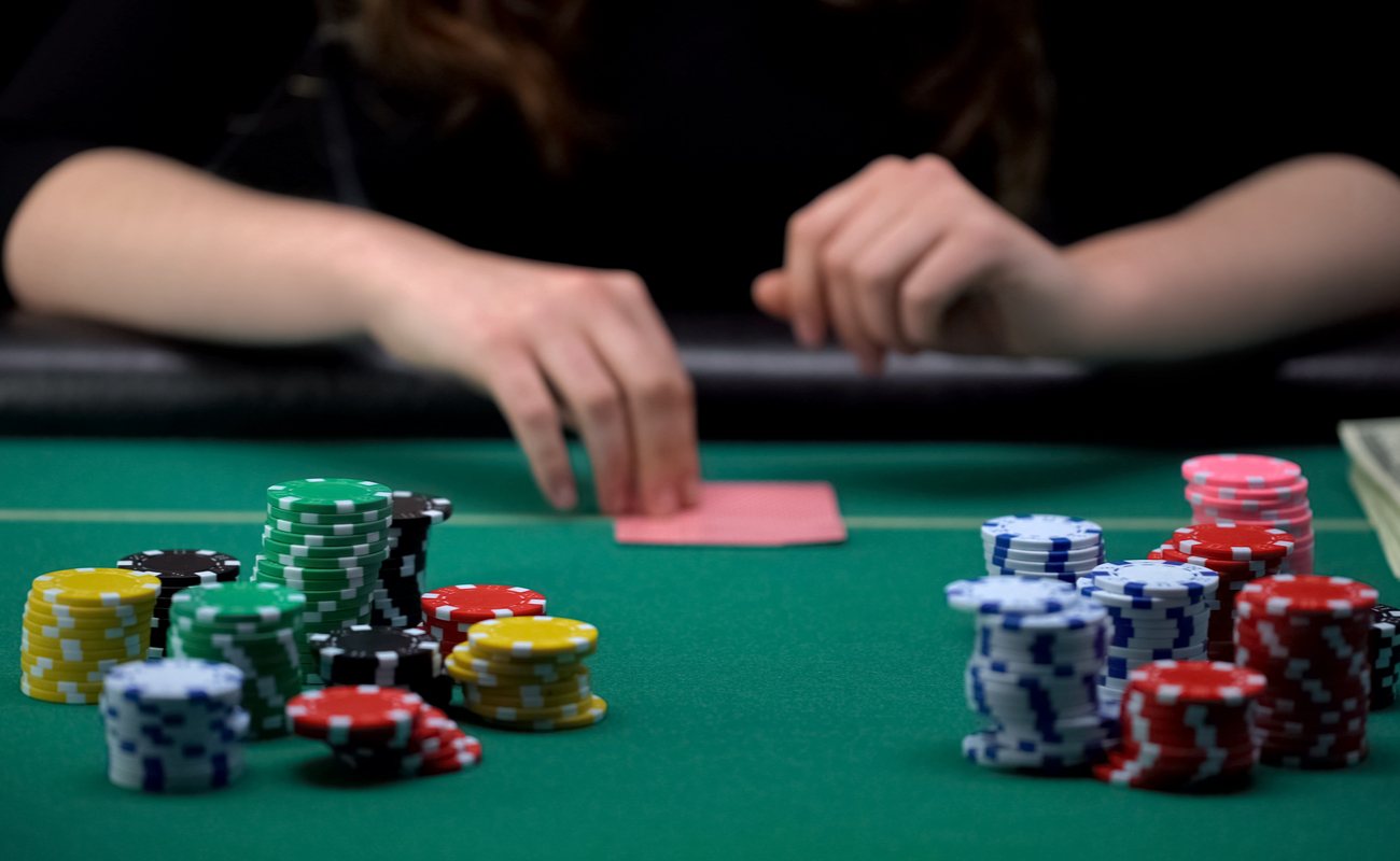 Woman playing poker at a casino table with chips and cards face down on the table.