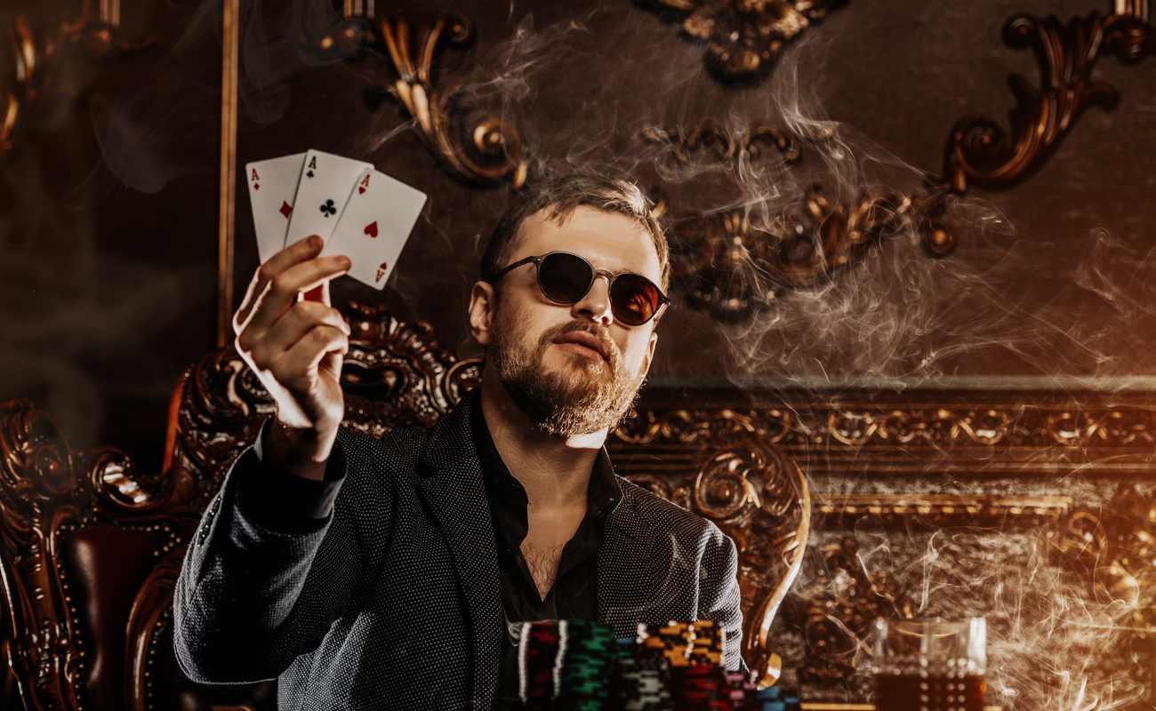 A well-dressed man holds up a winning poker hand with three aces.