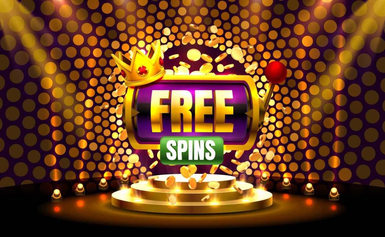 A 3D rendering of a slot machine with a crown and the words ‘free spins’ on it is seen sitting above a stage under spotlights.