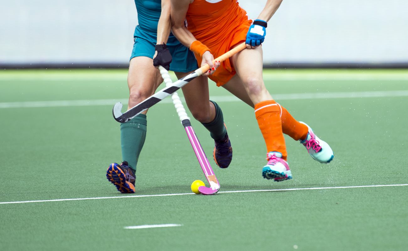 Two women playing a game of field hockey attempting to get the ball from each other.