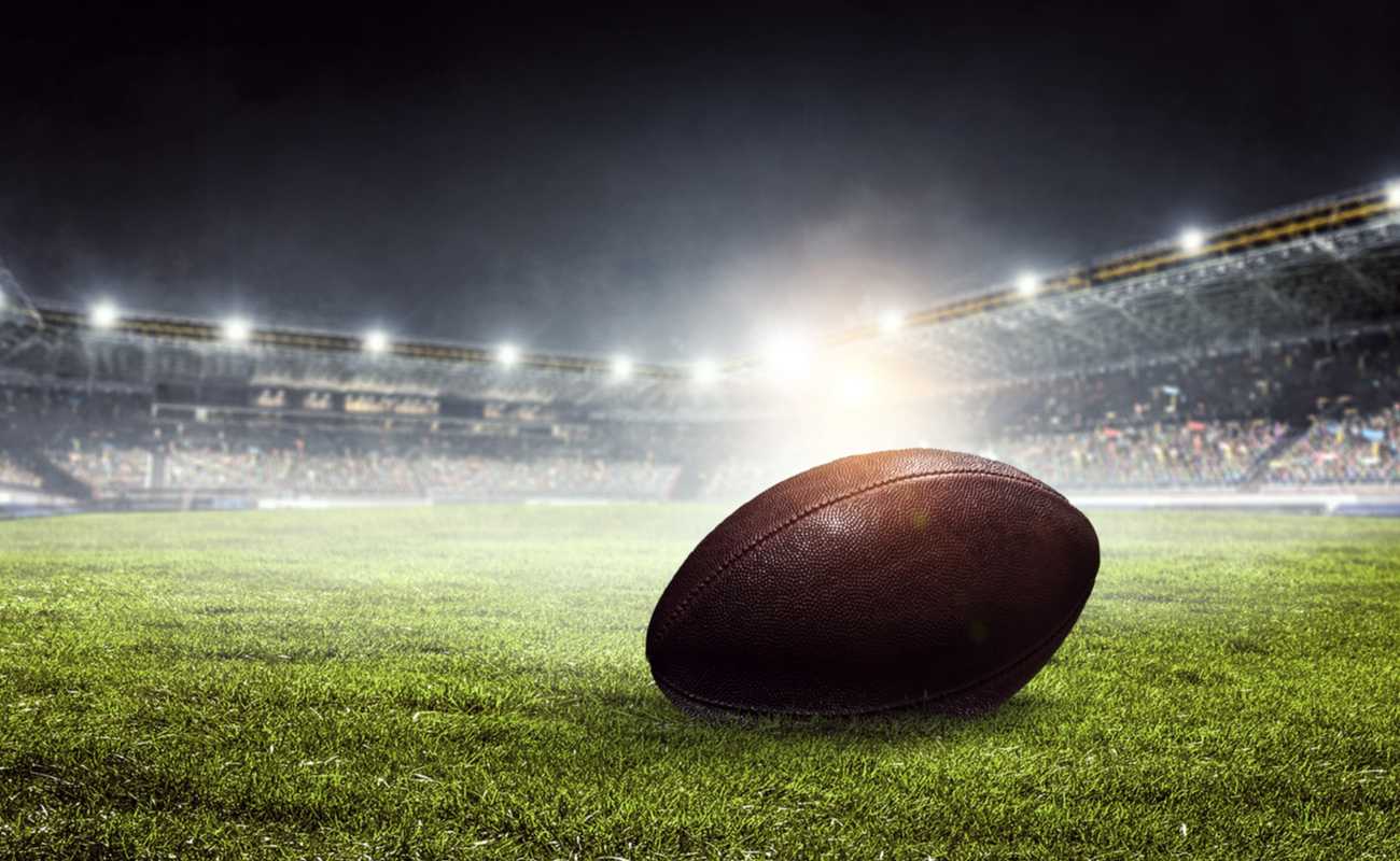 An American football lies on the field in a stadium.