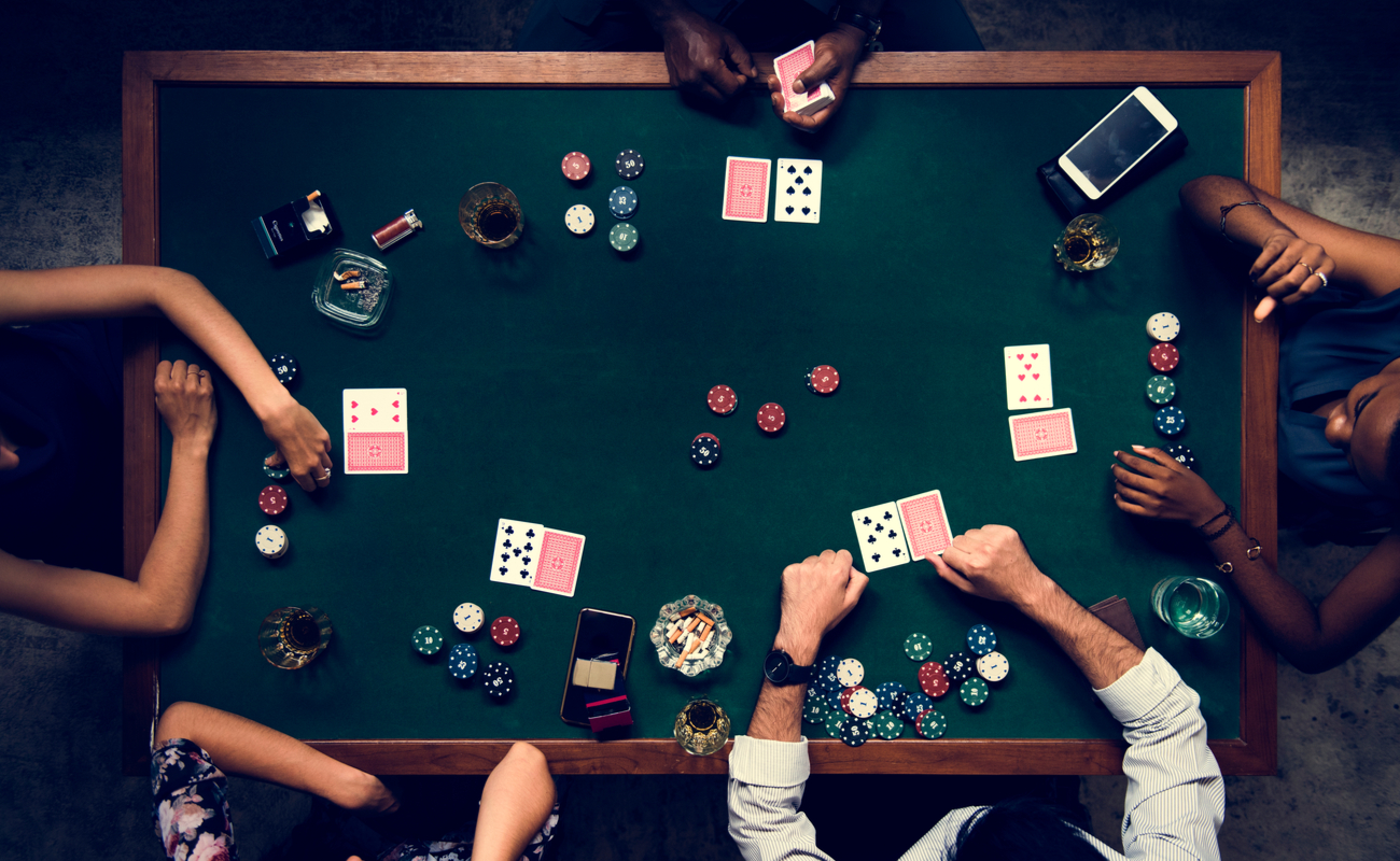 Aerial shot of five people playing poker with cards and chips at a casino table.