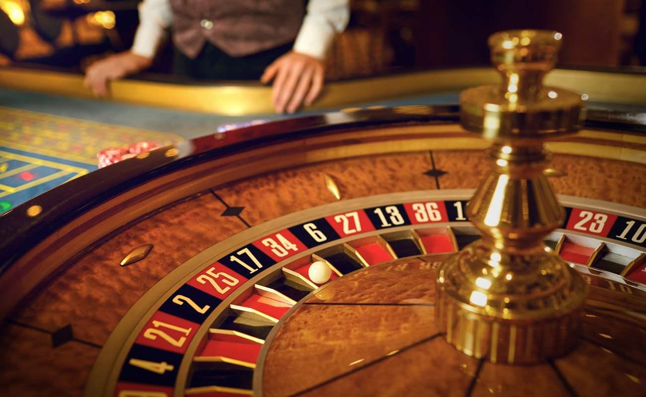 Dealer standing next to a roulette table and wheel with the ball landed on 34