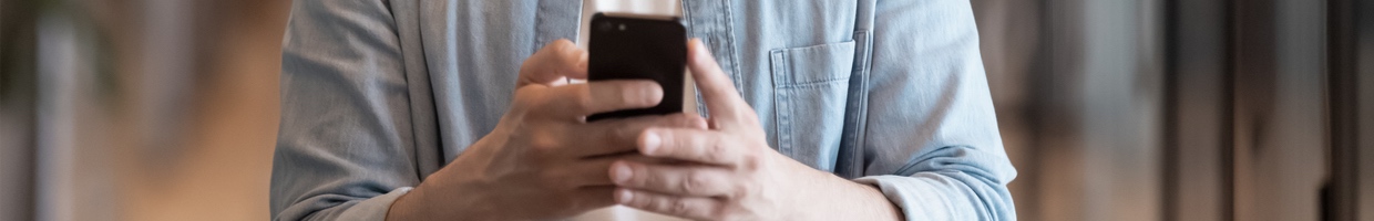 Young male employee in glasses smiling while looking at cellphone.