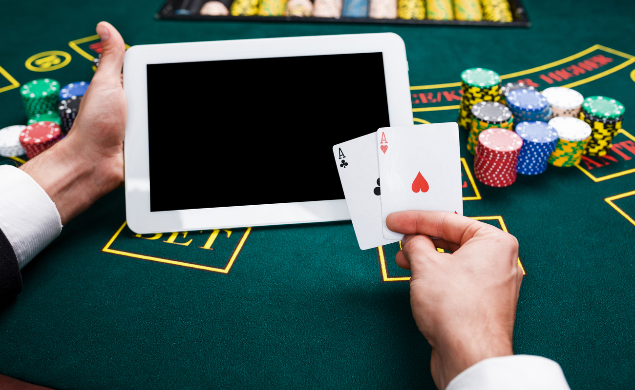  A man plays blackjack at a casino table with a tablet, a pair of aces, and casino chips.