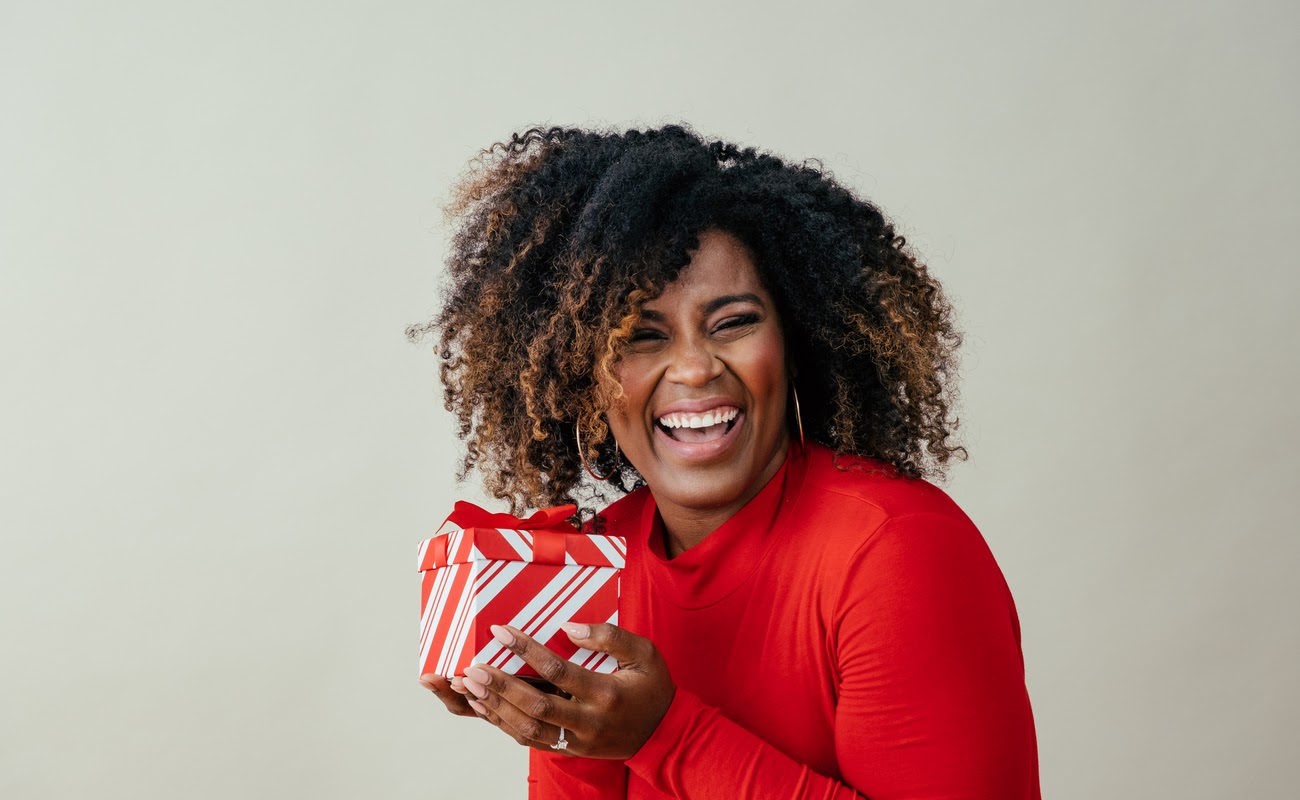 A happy woman in red receives a red and white gift box.