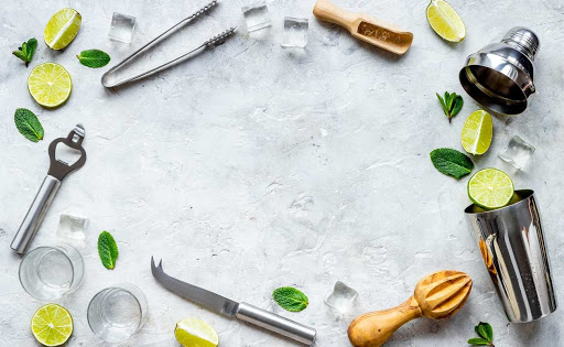 Cocktail-making tools displayed with mint leaves, ice, and lime slices.
