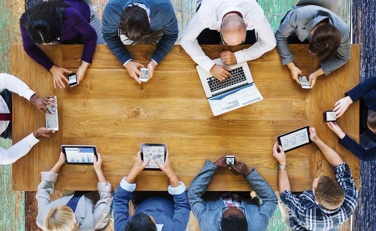 A group of people sitting around a table using various technological devices.