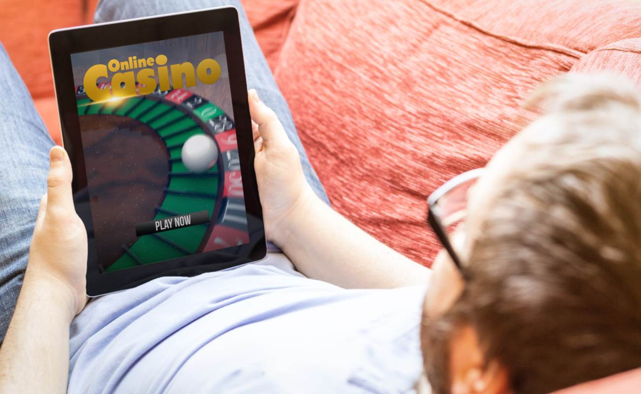 A man plays online casino games on his tablet while lying on his couch.