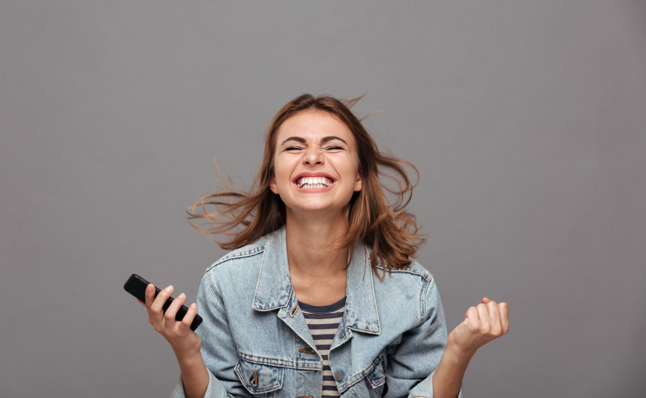 Close-up portrait of a woman holding a smartphone and celebrating a win.