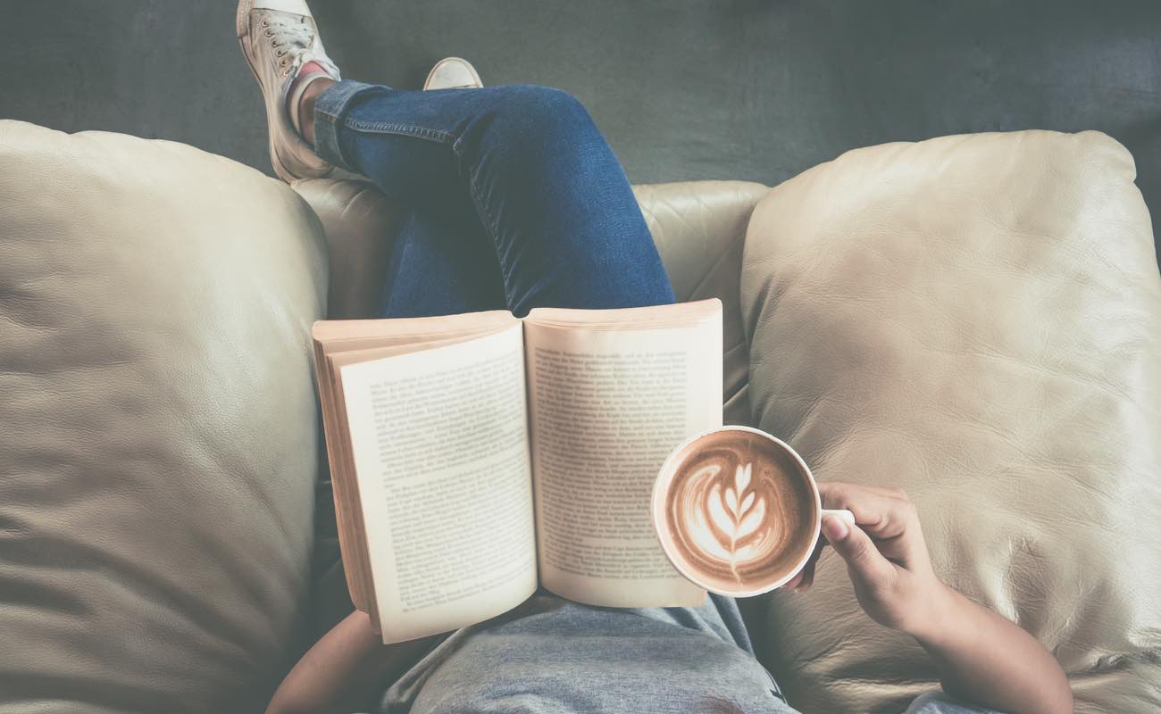 Top view of a woman reading a book and drinking coffee.