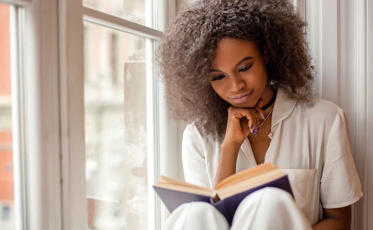 Women sitting on a windowsill, reading a book.