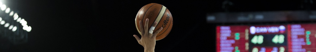 Player’s hand lifts basketball in dark background.