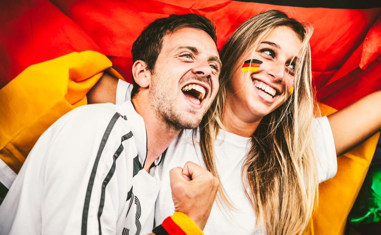 Soccer fans at a stadium with flags painted on their cheeks, cheering their teams