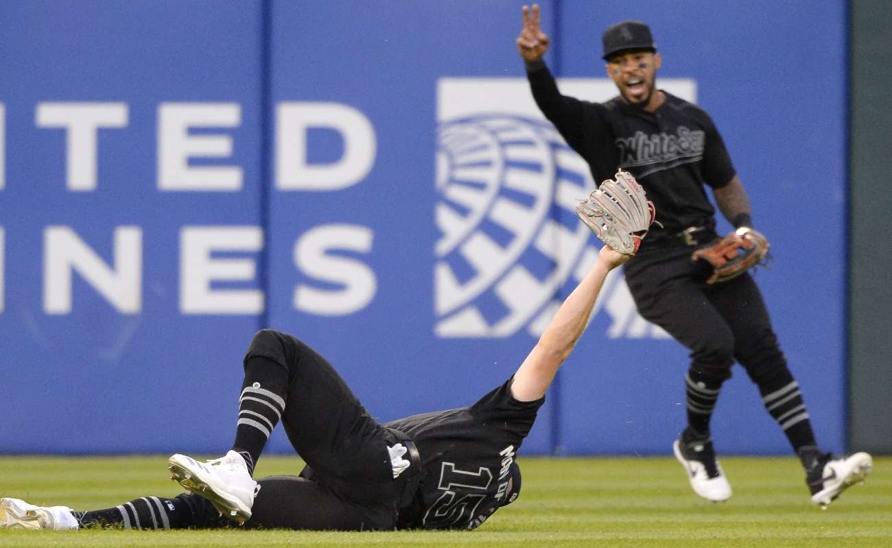 Baseball player Adam Engel of the Chicago White Sox makes a diving catch against the Texas Rangers and his teammate celebrates in the background.