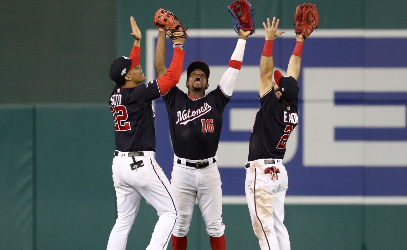 Washington Nationals players Juan Soto, Victor Robles, and Adam Eaton raising arms in the air.