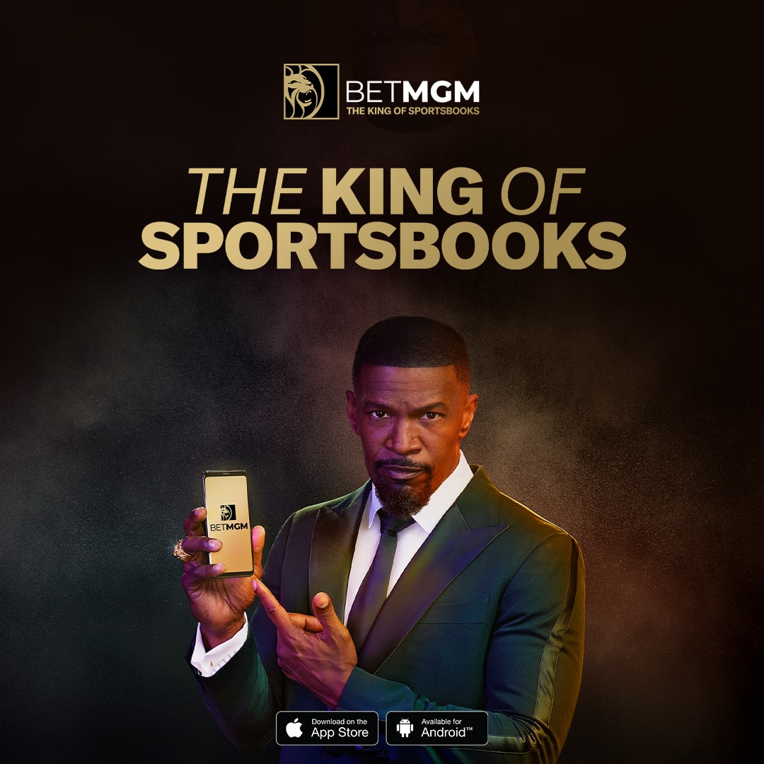 American portrait of actor and singer Jamie Foxx in a suit, holding a smartphone with a gold BetMGM background for the "The King of Sportsbooks" campaign