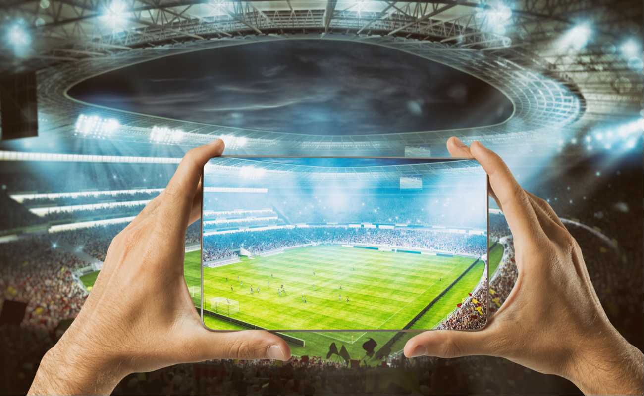 Hands holding a smartscreen mobile at football stadium watching sports live