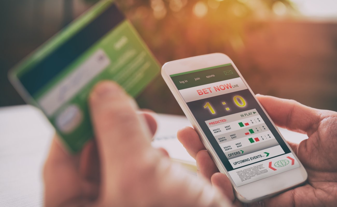 Man betting on sports with credit card, over shoulder view on hand with smartphone