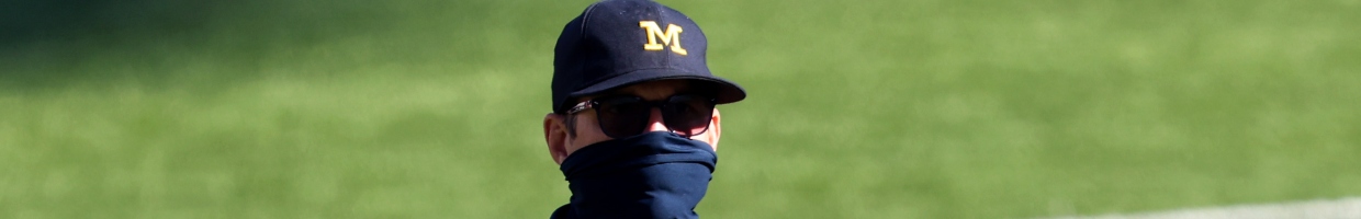 American football coach Jim Harbaugh wearing a black mask, sunglasses and a Michigan Wolverines football team cap